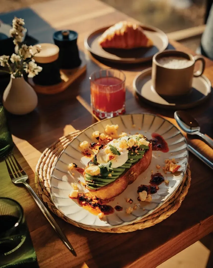 A breakfast table set with avocado toast, a pastry, coffee and juice