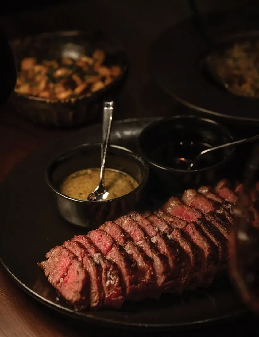 Sliced steak on a dark plate served with two sauces